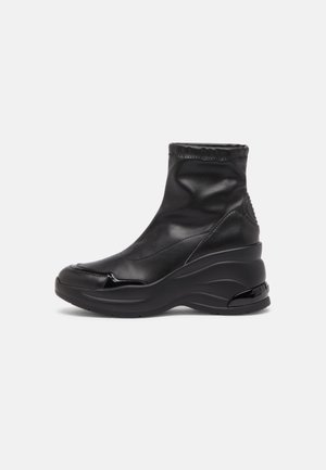 Sort ankelhøj sneakerstøvle med chunky sål, glat syntetisk overdel og diskret syningsdetalje på ensfarvet hvid baggrund.