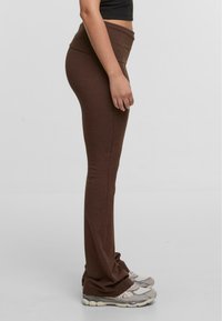 Barna, magas derekú leggings, puha, rugalmas anyagból készült. A leggings testhez álló fazonú, szürke sportcipővel párosítva.