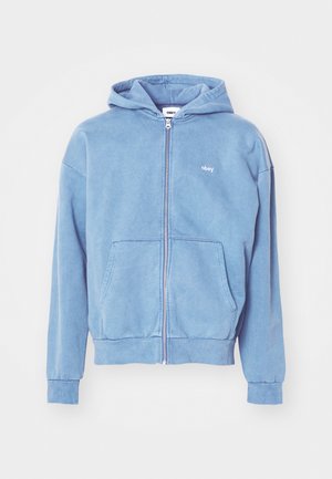 Light blue zip-up hoodie made of soft fabric, featuring a kangaroo pocket, ribbed cuffs, and a small white logo on the chest.