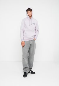 Light lavender hoodie with kangaroo pocket and drawstring hood, paired with loose-fitting gray jeans and black sneakers. Minimal design.