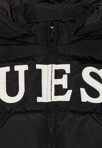 Giacca imbottita nera con logo "GUESS" ricamato in bianco sulla parte anteriore, con chiusura a zip e tessuto testurizzato.