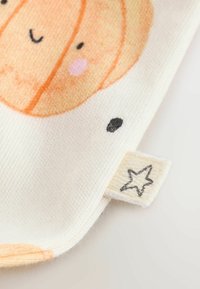 White fabric with an orange smiling pumpkin face, black dots, and a small beige tag featuring a black star outline.