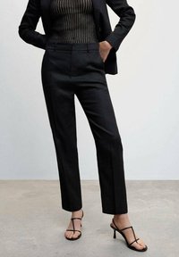 Černé kalhoty na míru se slim fit, hladkým povrchem, vysokým pasem a bočními kapsami, doplněné černými sandály na řemínky.