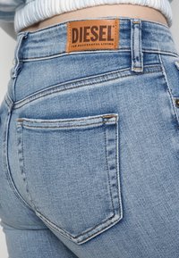 Jeans de mezclilla azul claro con cintura alta y bolsillos traseros. Cuenta con una etiqueta de cuero marrón "DIESEL" con texto grabado en la cintura.