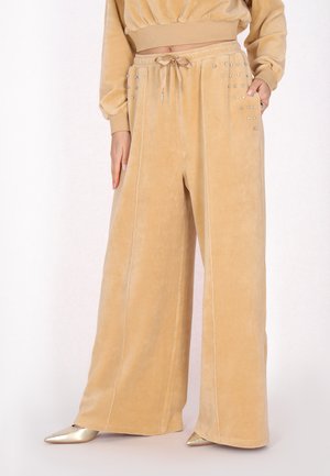 Beige Velour-Hose mit weitem Bein und Kordelzug in der Taille sowie kleinen Strasssteindetails an den Taschen, getragen mit einem passenden kurzen Top und goldfarbenen spitzen Schuhen.