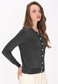 Cardigan nero glitterato con scollo rotondo, maniche lunghe e sei bottoni crema lungo la parte anteriore. Tessuto morbido e forma aderente.