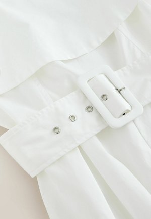 White fabric belt threaded through a rectangular buckle with metal eyelets on a white garment.