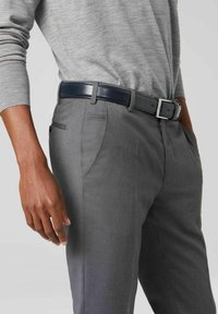 Graham-tailierte Hose mit Seitentaschen, kombiniert mit einem dunkelblauen glänzenden Gürtel mit einer silbernen Schnalle, getragen mit einem hellgrauen Strickoberteil.