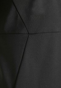 Svart klänning i tyg med en texturerad yta och geometriska sömmar och vinklar, som betonar rena linjer och en figurnära silhuett.