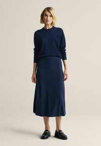 Laivastonsininen neulepaita ja siihen sopiva pitkä hame, molemmat sileää, hieman joustavaa kangasta. Pyöreä pääntie ja resorit hihansuissa; minimalistinen muotoilu.