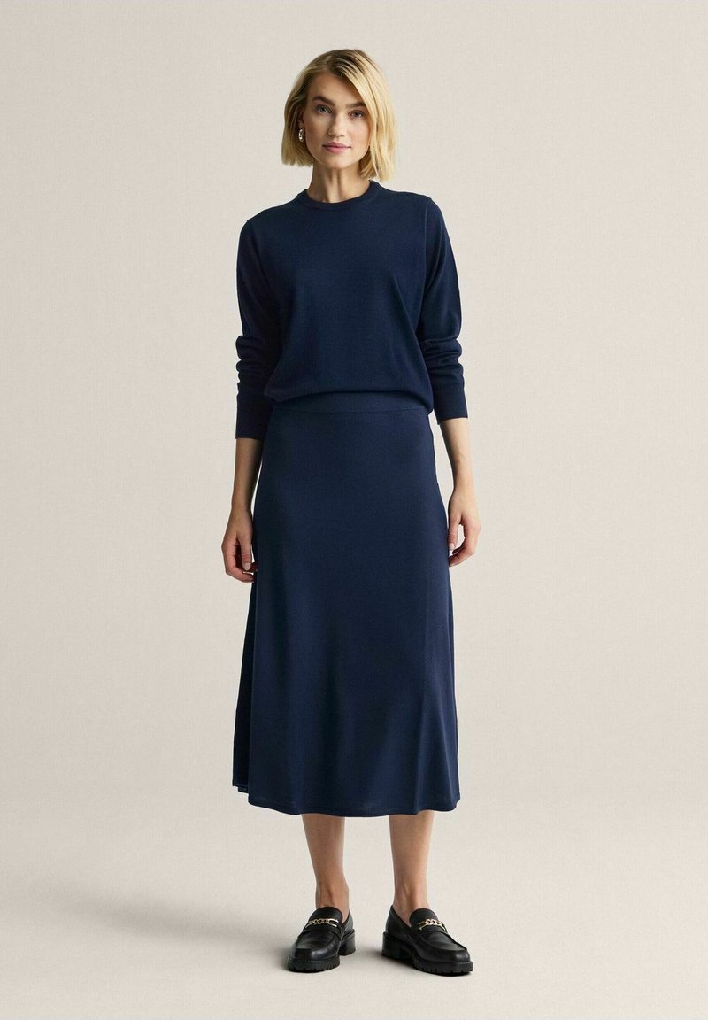 Laivastonsininen neulepaita ja siihen sopiva pitkä hame, molemmat sileää, hieman joustavaa kangasta. Pyöreä pääntie ja resorit hihansuissa; minimalistinen muotoilu.