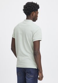 Polo in cotone verde chiaro con colletto classico, maniche corte e bordi bianchi a contrasto. Indossato con jeans blu scuri.
