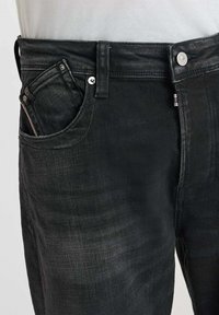 Jean en denim noir au design ajusté, avec une poche avant, une fermeture à bouton argenté et une texture subtile. Pas de motifs ou d'accents visibles.
