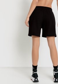Zwarte katoenen shorts met een elastische tailleband, met een relaxed fit en tot halverwege de dijen. Draagt met hoge sneakers en gestreepte sokken.