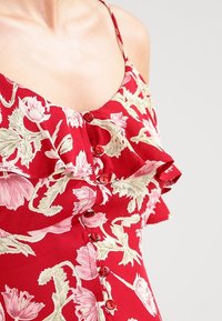 Rode jurk met bloemenprint, met een gerimpelde halslijn, knopen aan de voorkant en korte mouwen. De stof heeft een gladde structuur en voelt licht aan.