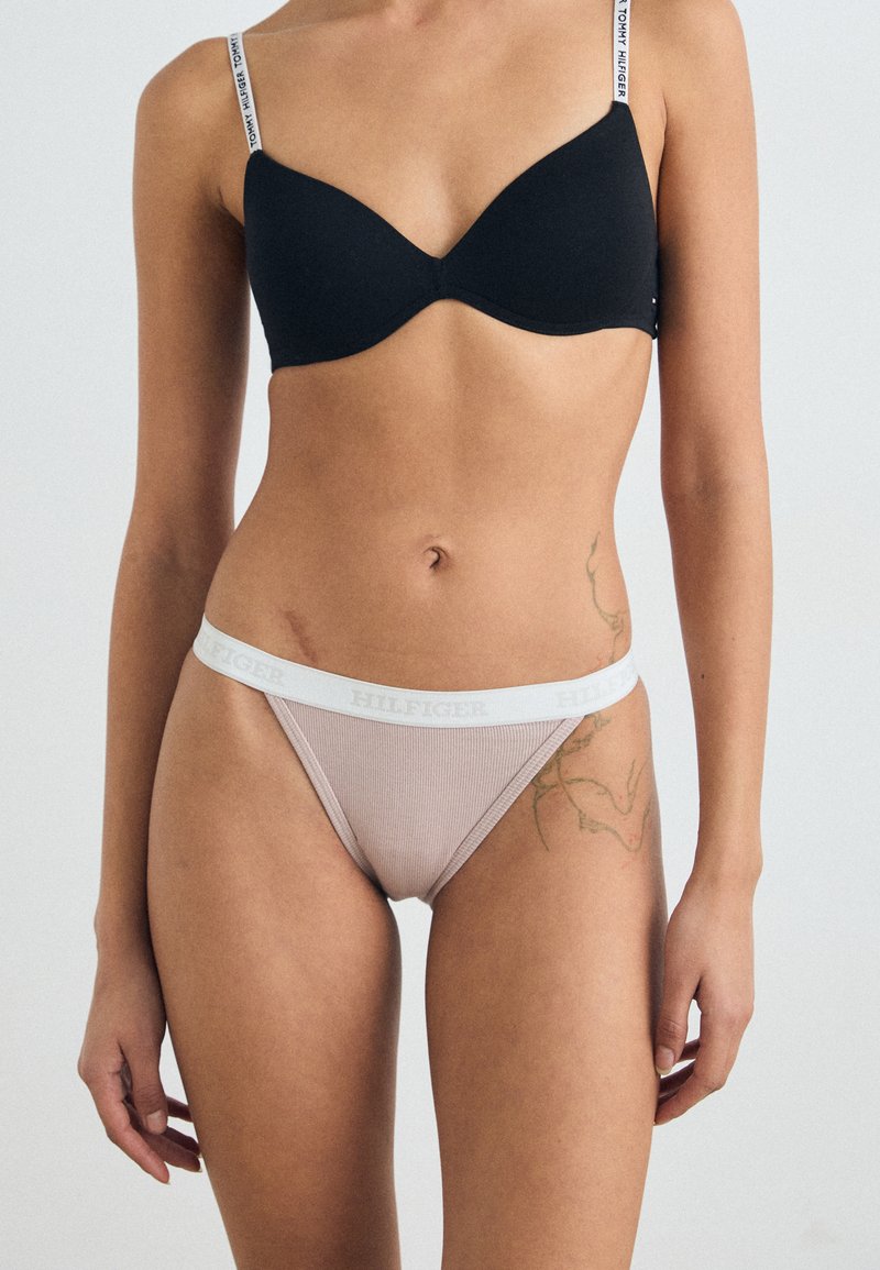 Sutien padding negru și thong roz deschis, cu nervuri, având un brâu alb cu branding "HILFIGER". Textură netedă, design ajustat.