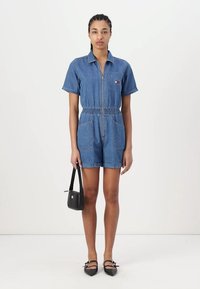 Denim overal na krátko se zapínáním na zip, límečkem a elastickým pasem; má dvě přední kapsy a malé logo na hrudi.