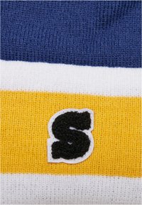 Secțiune de pulover tricotat cu dungi orizontale bleumarin, albe și galbene. Include un logo negru din fetru cu litera "S" pe un fundal alb. Material texturat.
