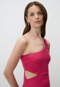 Robe asymétrique rose en tissu texturé avec des découpes sur le côté, accompagnée de boucles d'oreilles en mosaïque colorées.