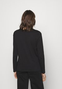 Musta pitkähihainen paita, jossa on pyöreä kaula-aukko ja pehmeä rakenne. Ominaisuuksiin kuuluu rento istuvuus ja yksinkertainen muotoilu, kuvattu takaviistosta.