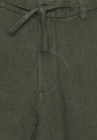 Tmavě zelené kalhoty vyrobené z texturované látky s šňůrkovým zapínáním a knoflíkovým detailem na pase. Mají přední kapsy.