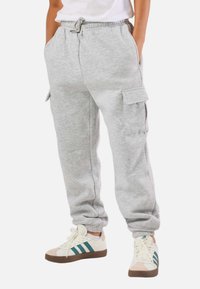 Person wearing light grey cargo sweatpants with elastic ankles and pockets, paired with white sneakers with teal stripes and gum soles.