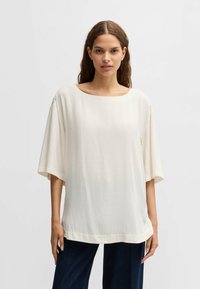 Top bianco, ampio e comodo realizzato in un tessuto liscio e leggero. Presenta un ampio scollo rotondo e maniche scese. Orlo semplice.