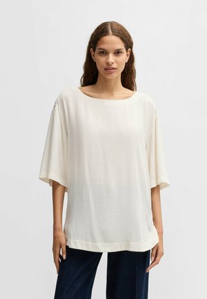 Top bianco, ampio e comodo realizzato in un tessuto liscio e leggero. Presenta un ampio scollo rotondo e maniche scese. Orlo semplice.