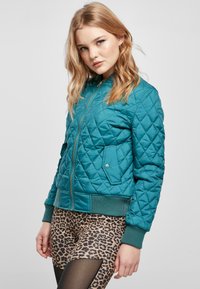 Teal quiltad bomberjacka med dragkedja fram, ribbade muddar och två sidofickor. Matchas med leggings i leopardmönster.