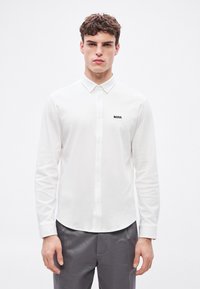 Biela košeľa s dlhým rukávom na gombíky, vyrobená z bavlny, s golierovým výstrihom a malým čiernym logom "BOSS" na hrudi.