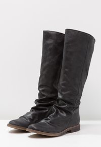 Bottes en cuir noir montantes jusqu'au genou avec une texture froissée, des bouts arrondis et des talons bas en caoutchouc marron. Design simple avec des accents minimalistes.