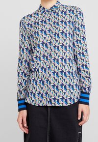 Napapaita, jonka pohjaväri on laivastonsininen ja jossa on värikäs "LOVE"-kuvio. Hihansuut ovat siniraidalliset, paidassa on kaulus ja pitkät hihat.