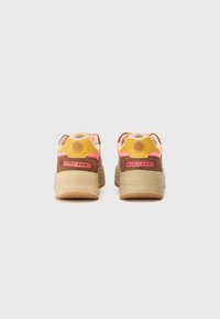Sneaker marroni e gialli con accenti rosa, dotati di una suola in gomma testurizzata, colletto imbottito e dettaglio del logo sul retro.