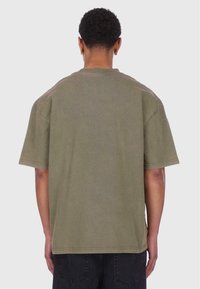 Oliven grøn oversized T-shirt med korte ærmer og rund hals. Blød tekstur, enkelt design og minimale syninger.