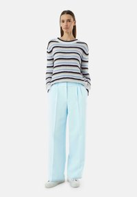 Sweter w paski w kolorze niebieskim, białym i granatowym o luźnym kroju; zestawiony z jasnoniebieskimi spodniami w szerokiej nogawce oraz białymi sneakersami.