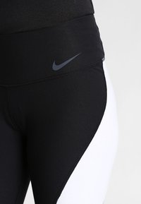 Leggings sportivi nero e bianco con vita alta, con logo Nike in vita. Realizzati in un tessuto elasticizzato con una superficie liscia.