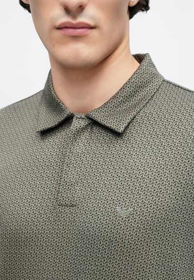 Polo en tissu texturé kaki avec un motif géométrique subtil. Comprend un col classique et un petit logo brodé au-dessus de la poitrine.