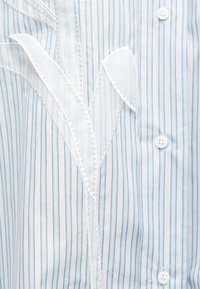 Πουκάμισο με γαλάζιες και λευκές ρίγες, με κεντημένη λευκή λουλουδάτη απλικέ και λευκά κουμπιά κατά μήκος του μπροστινού μέρους.