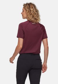 Burgundisk kortärmad skjorta med raglanärmar, paret med svarta byxor som har en dragkedjeficka. Slät textur, atletisk passform.