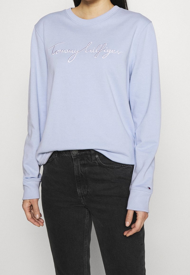 Sweat-shirt à manches longues bleu clair en matière douce, avec le logo "Tommy Hilfiger" brodé sur la poitrine et des poignets côtelés.