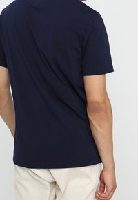 Námorně modré bavlněné tričko s krátkými rukávy, kulatým výstřihem a volným střihem. Hladká textura s minimálním detailem na zadní straně.