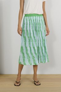 Svijetloplava nabirana suknja s zelenim tie-dye uzorkom, elastičnom waistline, i dužinom do gležnjeva. Nosena s crnim japankama na drvenom podu.