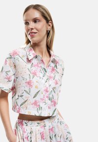 Blomstret cropped skjorte i let stof med lyserøde og hvide blomstermønstre, grønne blade og en kort krave. Knaplukning detaljer.