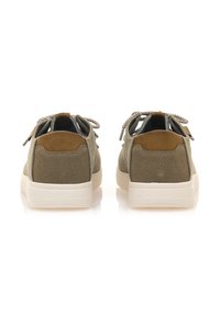 Zapatillas de lona verdes con detalles de cuero marrón, cordones redondos y suelas de goma beige. Presentan una superficie texturizada y un diseño de perfil bajo.