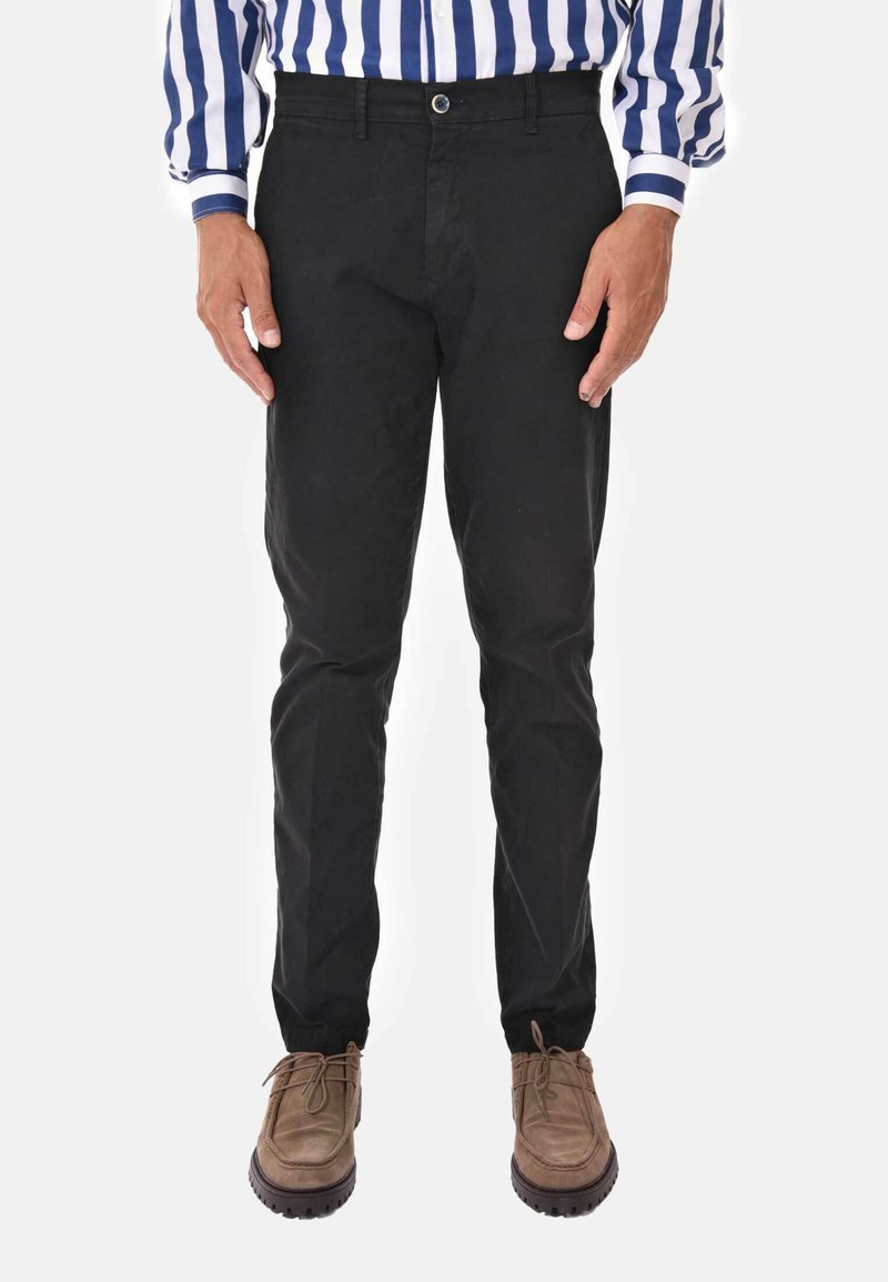 Pantaloni neri in cotone con vestibilità dritta, chiusura con cerniera e bottone. Abbinati a scarpe marroni, vista frontale senza dettagli aggiuntivi.