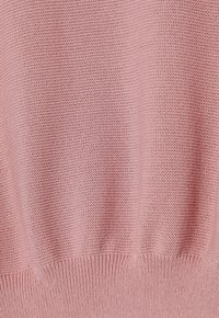 Gros plan d'un tissu tricoté rose à tissage serré avec un ourlet côtelé en bas.