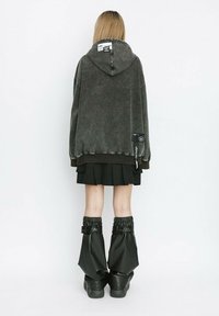 Sudadera de forro polar gris de gran tamaño con capucha ajustable, falda corta negra y botas de tobillo negras brillantes con puños elásticos.