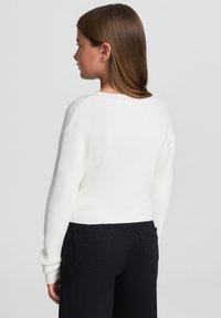 Biały sweter z prążkowanej tkaniny o skróconym kroju i długich rękawach, w połączeniu z czarnymi spodniami z tylnymi kieszeniami.