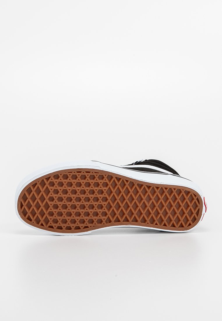 Suela de zapatilla en blanco y negro con un patrón de agarre de goma texturizada, que presenta un diseño de espiga marrón y bordes laterales blancos.