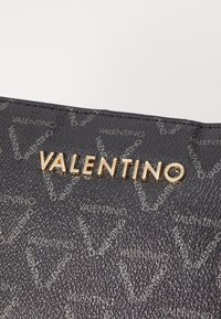 Czarny portfel z teksturowanej skóry z złotym logo „VALENTINO” oraz tłoczonym wzorem nazwy marki na powierzchni.